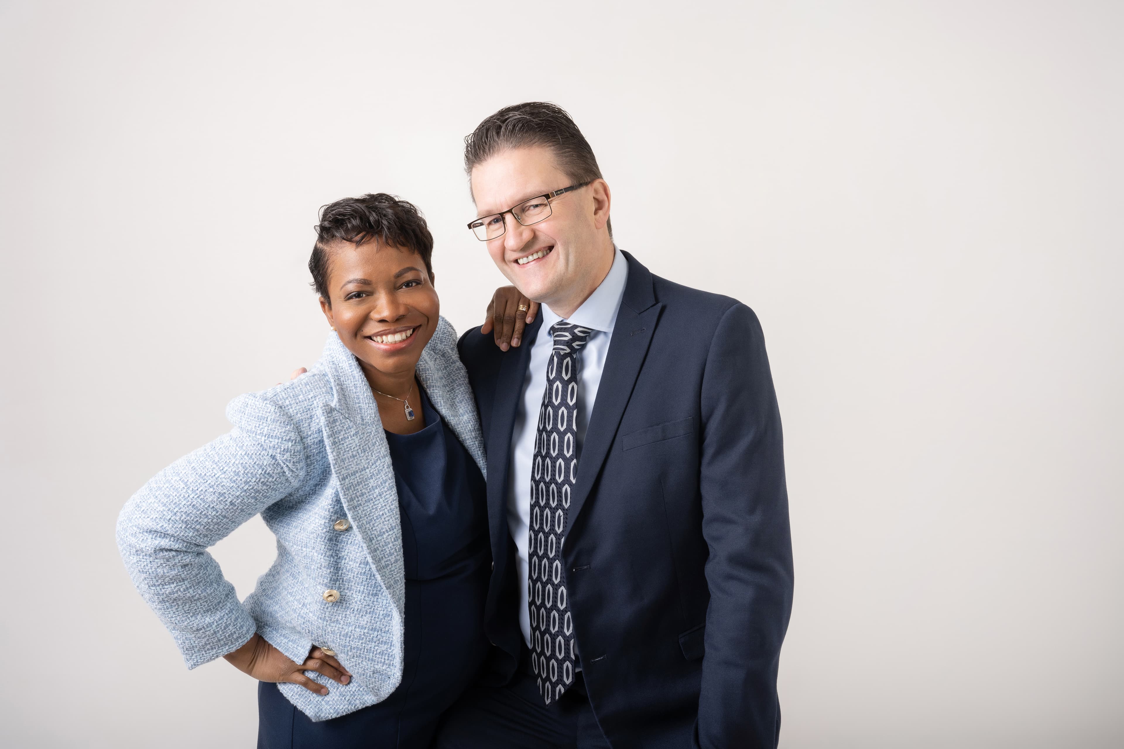 Smiling Black woman in light blue blazer and white man in dark suit posing together.